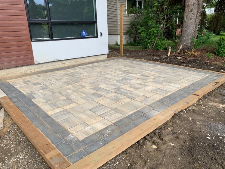 Newly installed paver patio with contrasting dark border beside house